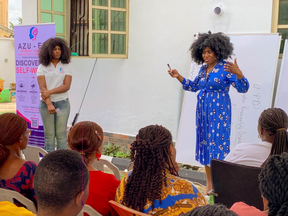 Azu-Eri session outdoors, with a facilitator speaking to a seated group beside the foundation banner